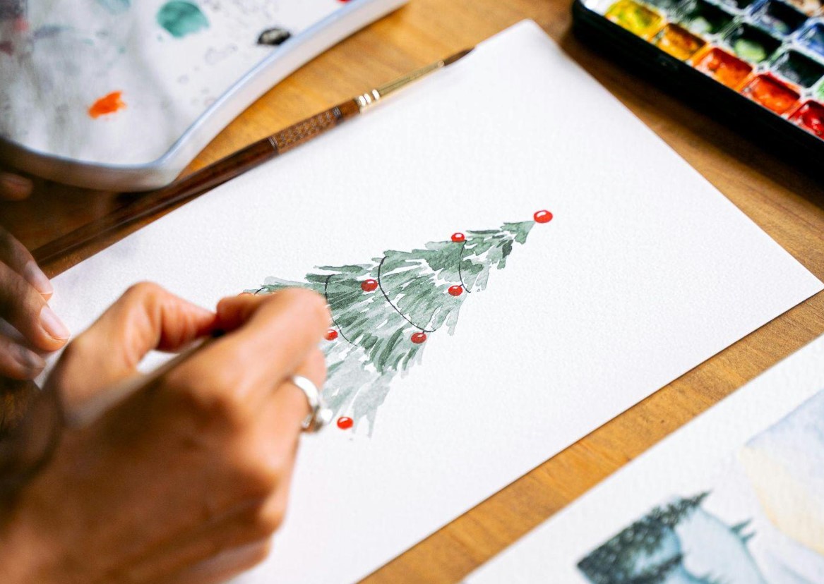 Someone is drawing Christmas tree on a piece of paper, close-up